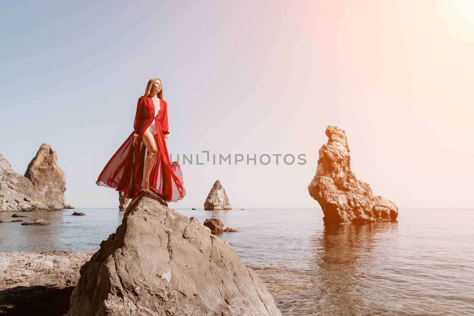 Woman travel sea. Young Happy woman in a long red dress posing on a beach near the sea on background of volcanic rocks, like in Iceland, sharing travel adventure journey by panophotograph