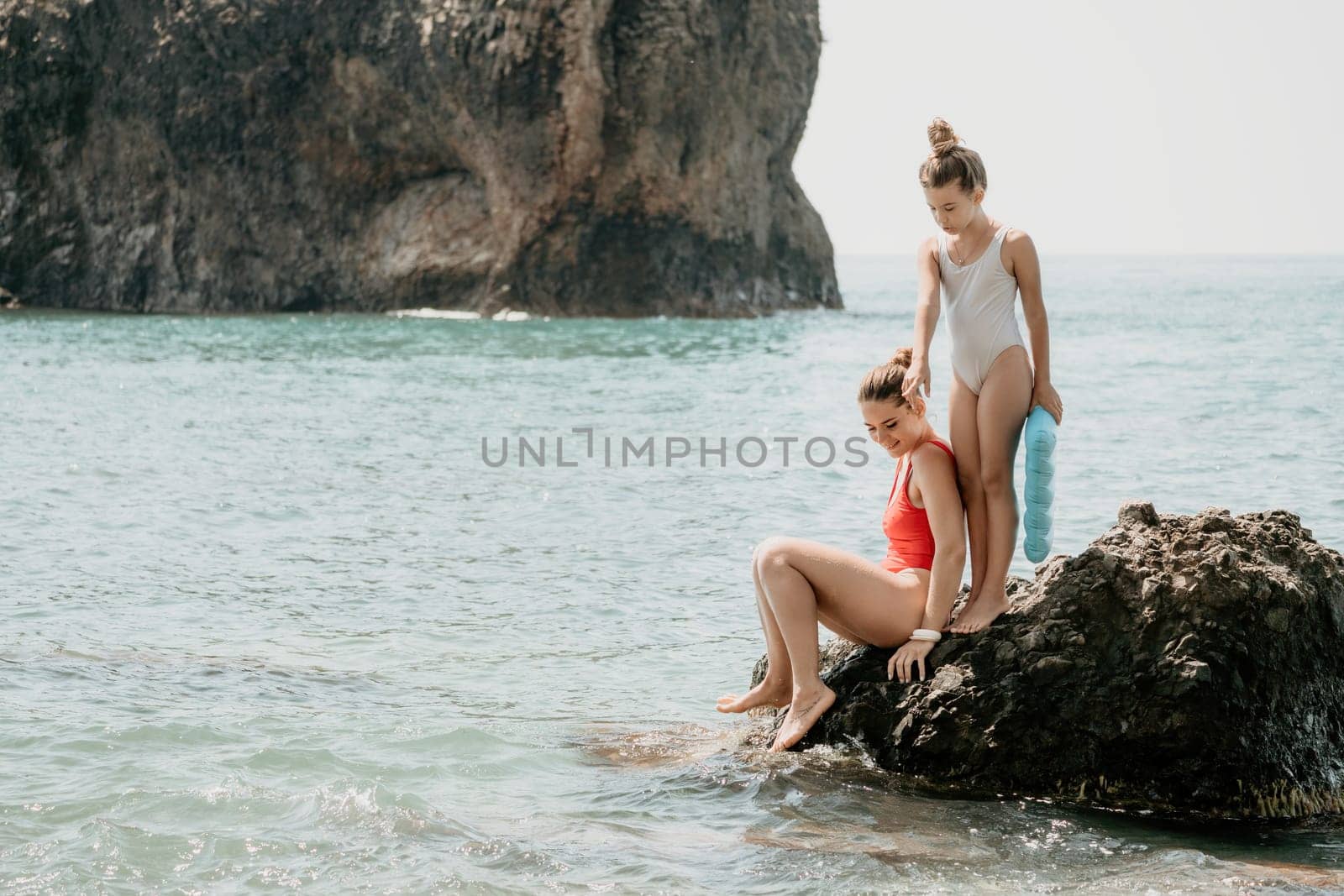 Woman and her daughter together on rock in the sea.