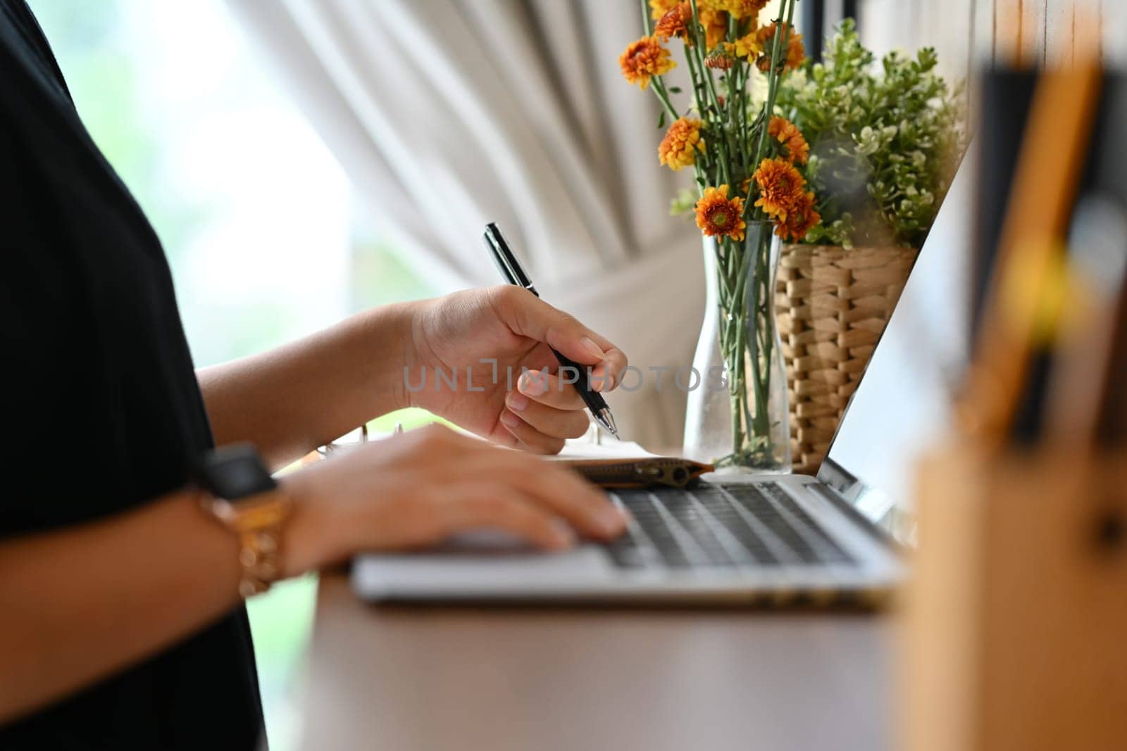 Side view of young woman using laptop computer and writing in a notebook by prathanchorruangsak