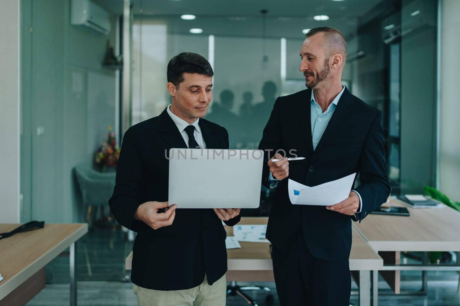 Two business men meeting to talking or discuss marketing work in workplace using paperwork, calculator, computer to work. by Manastrong