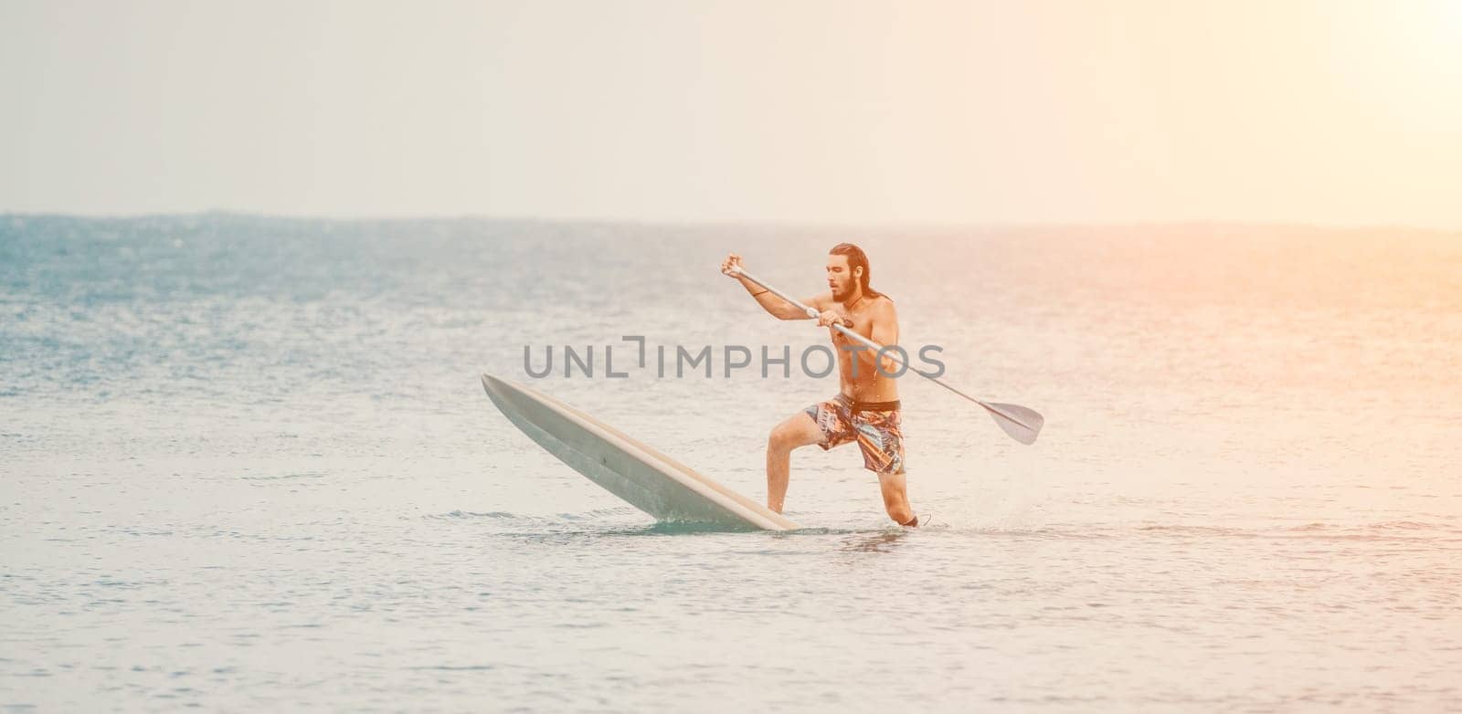 Sea man sup. Asian athlete man swimming in sea and paddleboarding at summer sunset. Healthy strong male enjoy outdoor active lifestyle and water sports on holiday vacation. by panophotograph