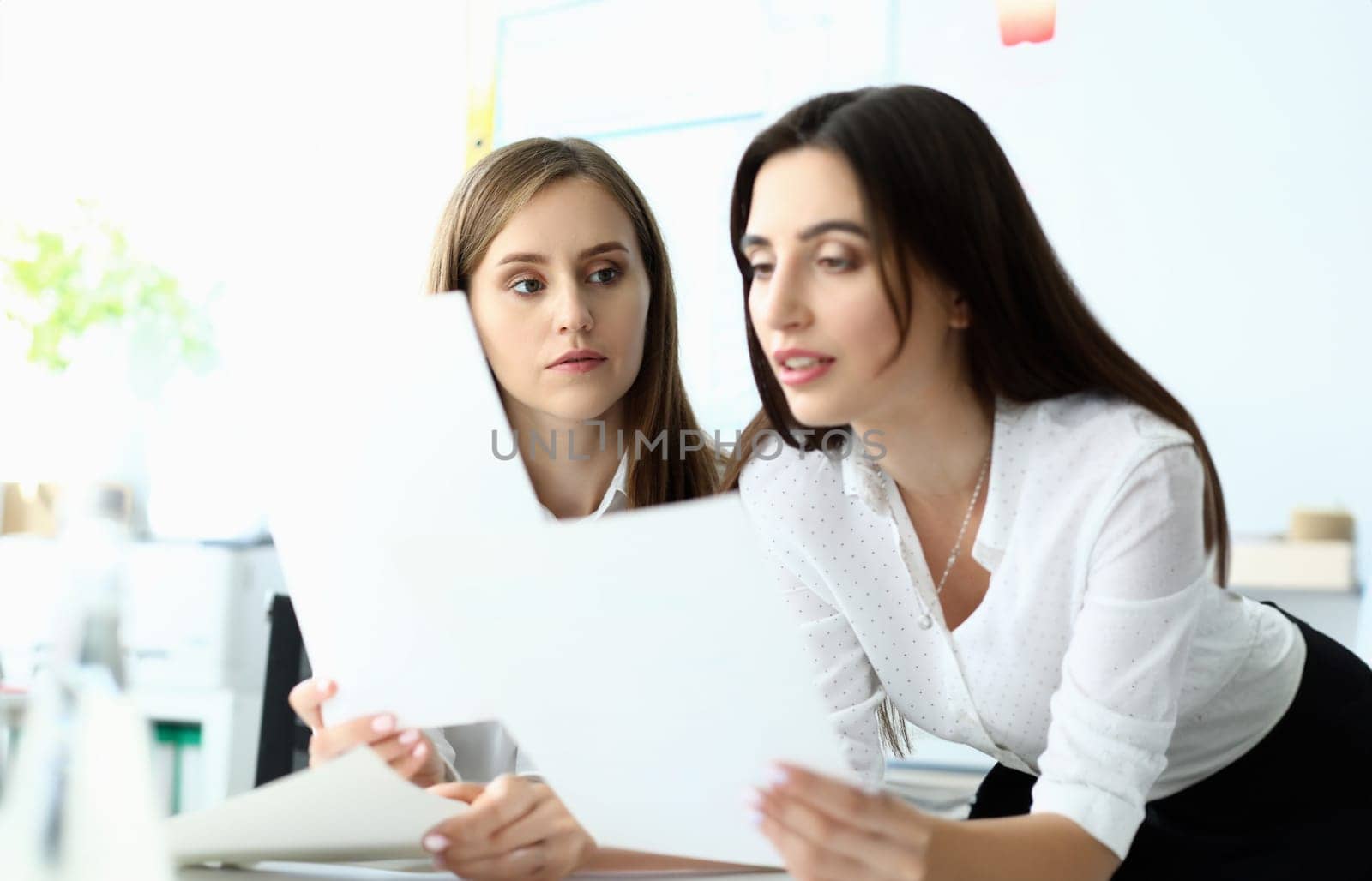 Portrait of smart businesswoman looking at important document with significant information about company profit and standing near concerned colleague. Accounting office concept