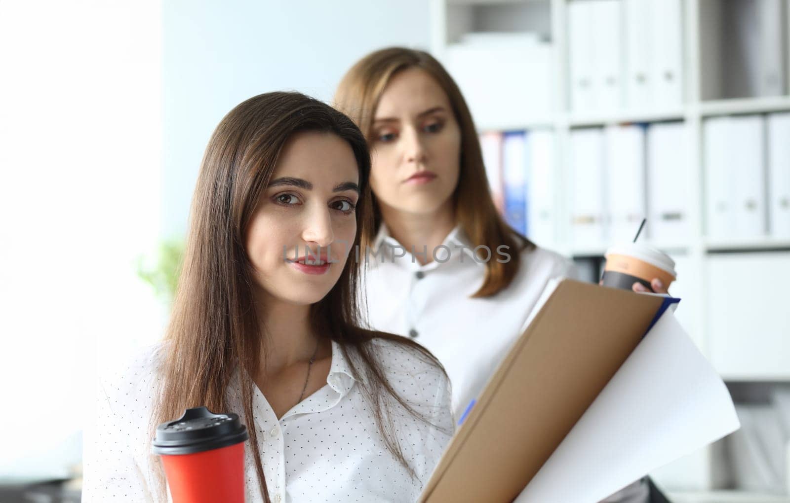 Portrait of pretty businesswoman holding important tablet with biz documents and working with smart friendly female colleague. Accounting office concept