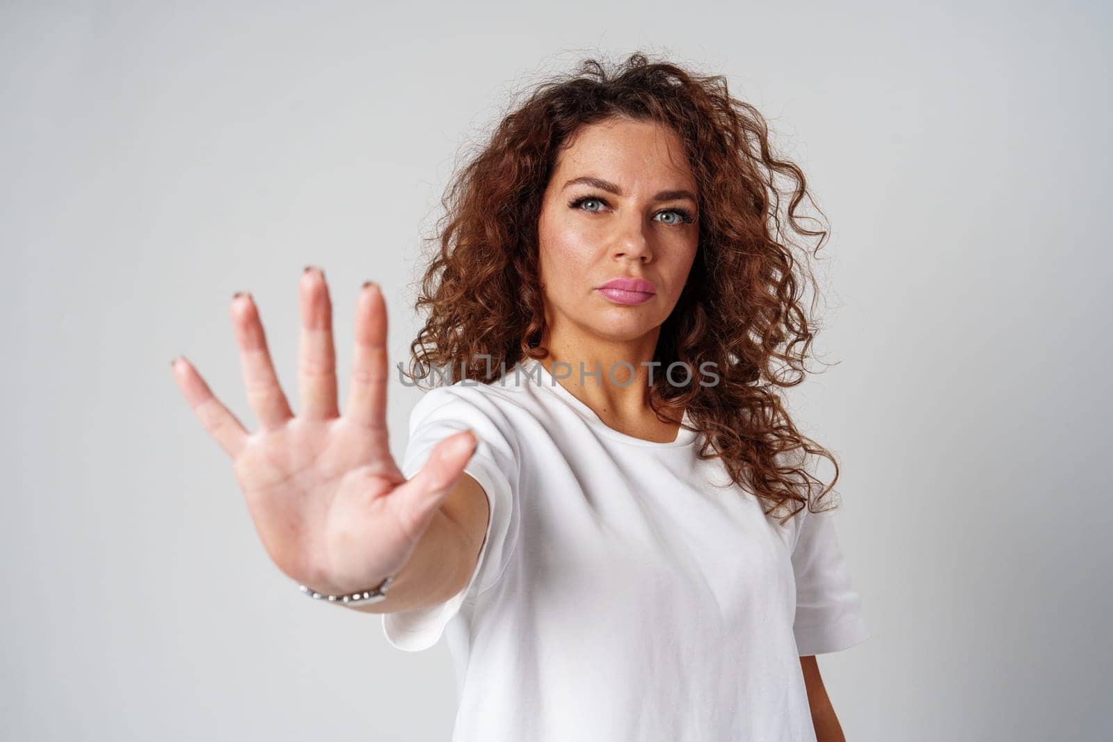 Woman with curly hair making a stop gesture in a studio against a plain background close up