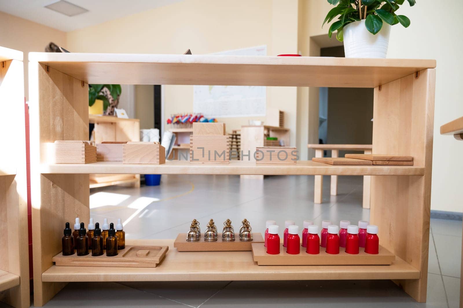 Organized Montessori classroom shelf featuring educational materials like wooden blocks, bells, dropper bottles, and red liquid containers for hands-on learning.