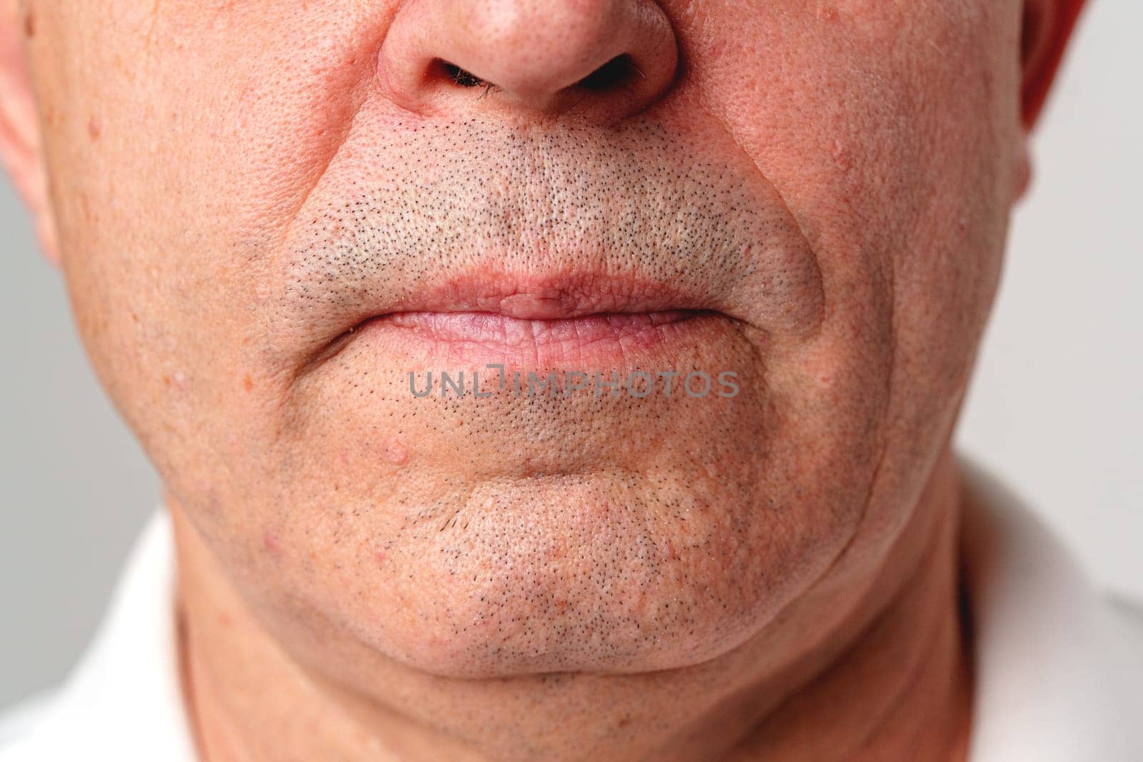 Close-up view of an older man's chin and mouth area against a neutral background