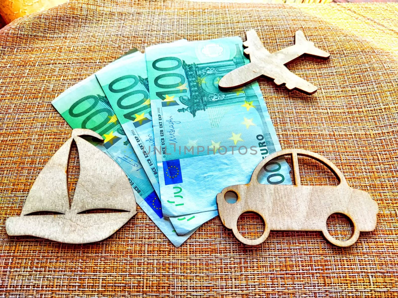 Three wooden shapes representing transport are arranged alongside euro bills, illustrating cost comparisons for travel options.