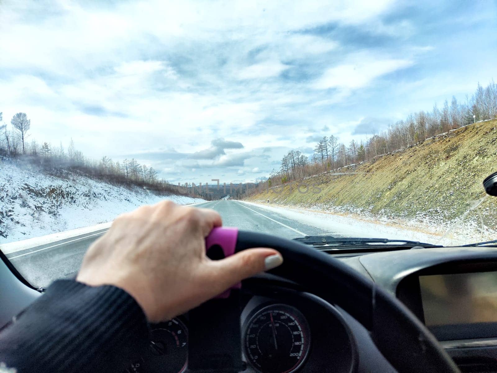 Car salon, windshield, hand of woman on steering wheel and landscape. View from seat of driver on nature landscape. Single trip of female traveler