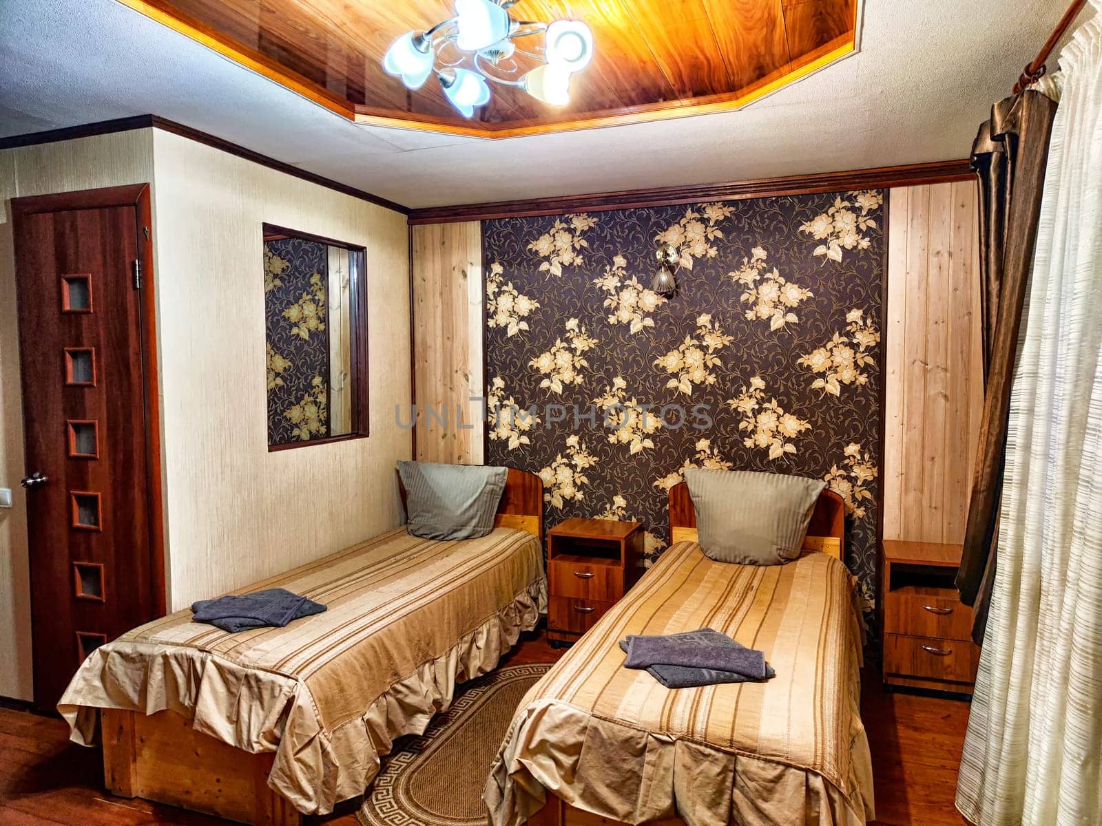 This welcoming twin bedroom features floral wallpaper and wooden accents, offering a cozy atmosphere with ample natural light and comfortable bedding.