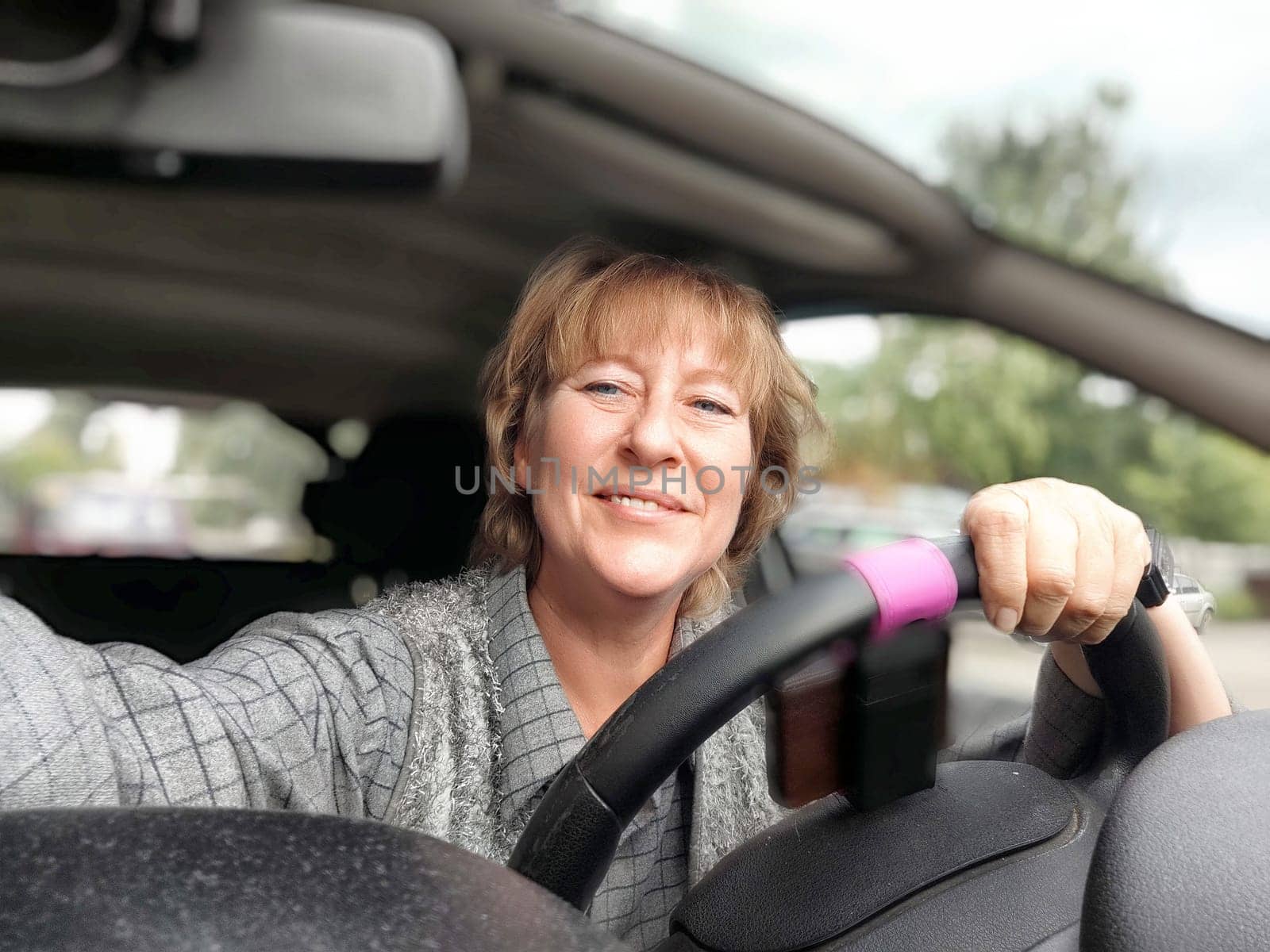 A middle aged woman is happily smiling as she drives her car, enjoying the sunny day outside.