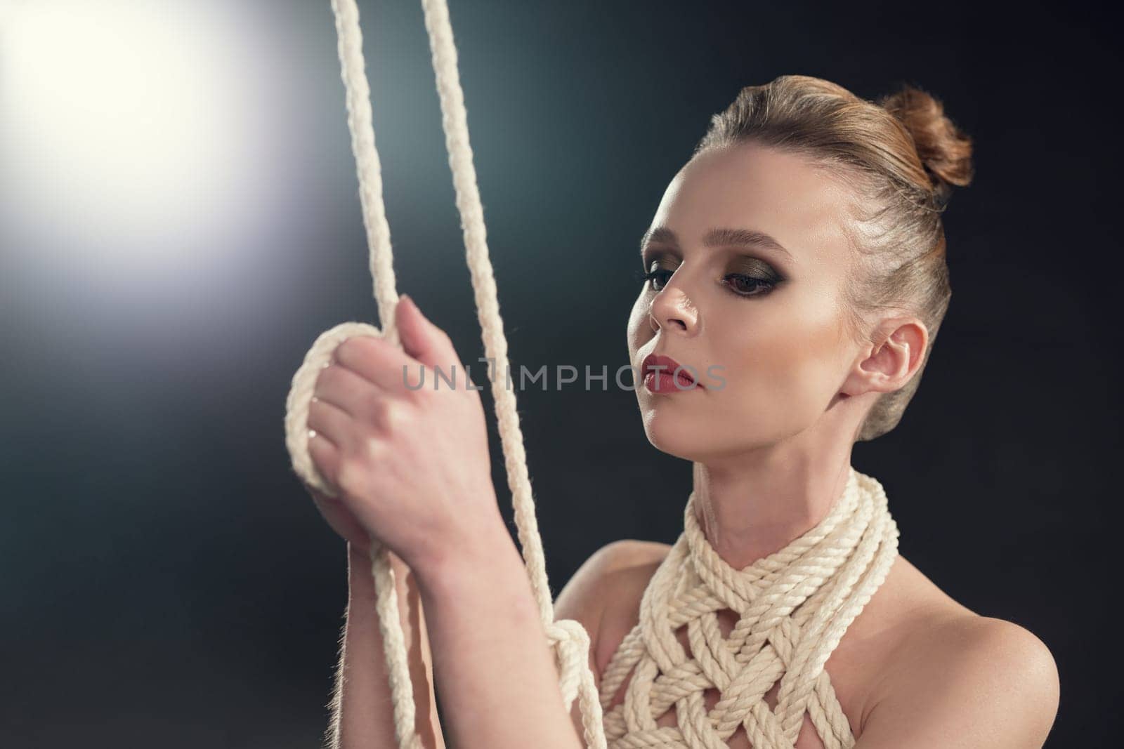 Beautiful naked woman tied up with rope portrait against black wall