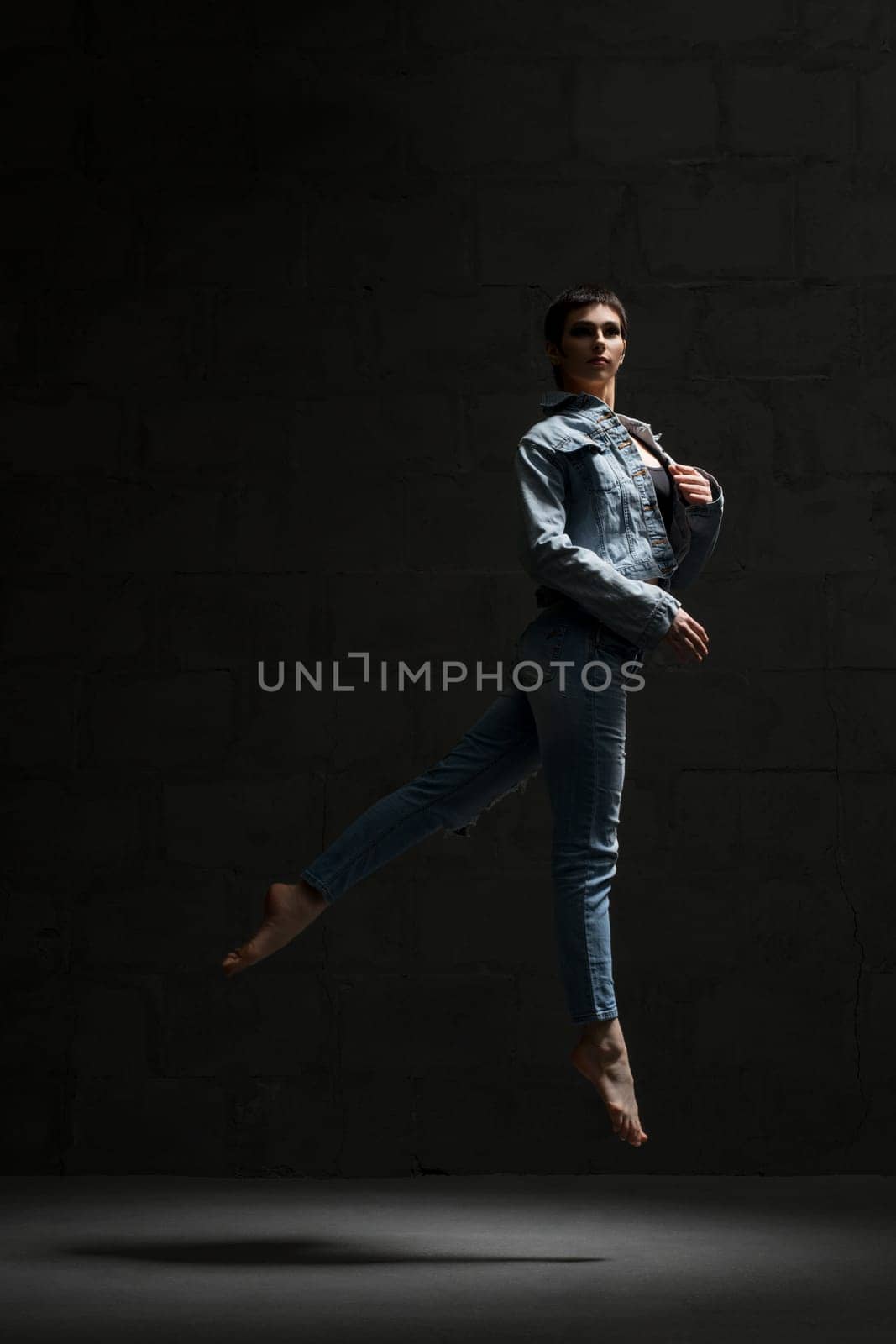 Ballet dancer with shot haircut in jeanswear jumping gracefully in dark room