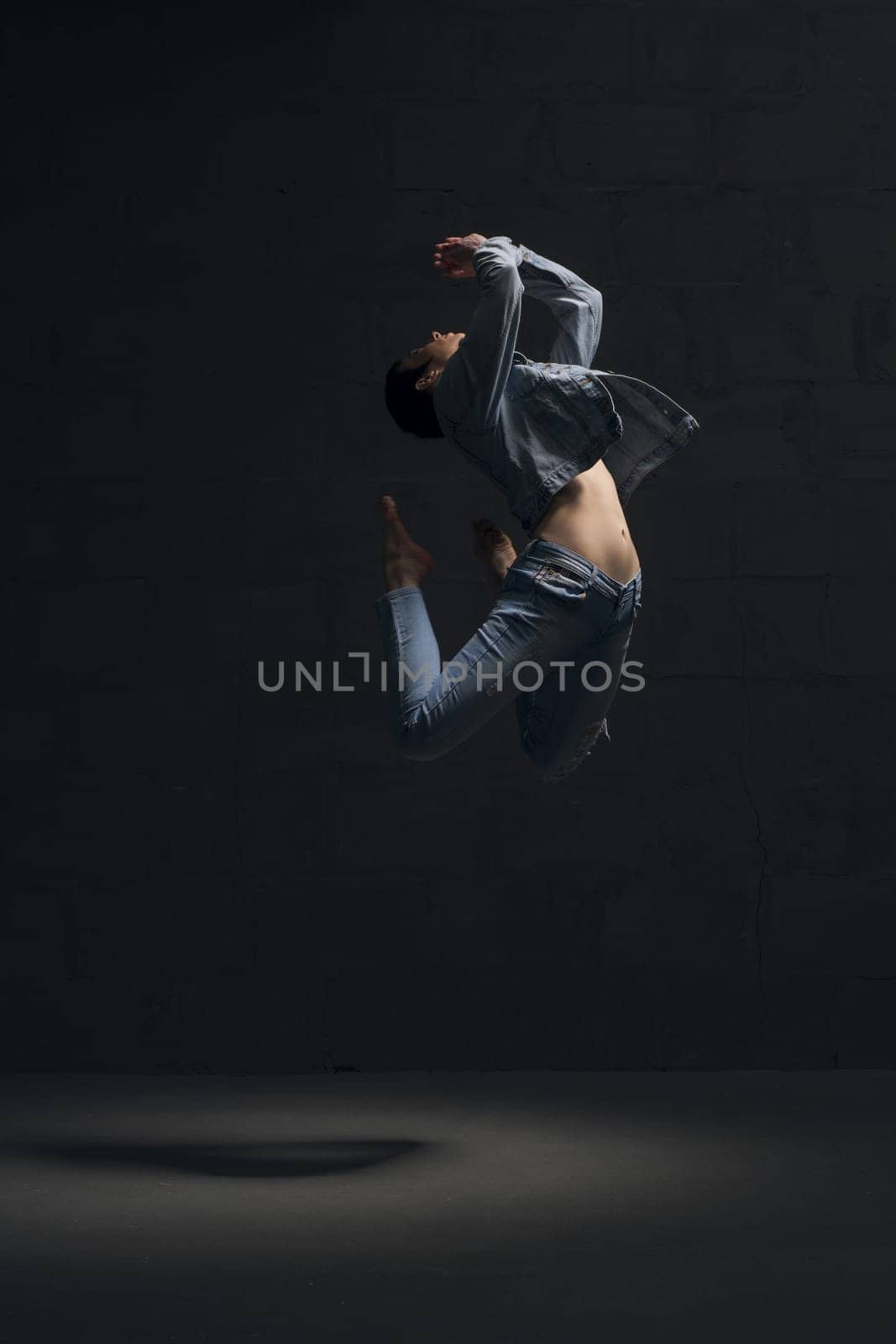 Girl with shot haircut in jeanswear dancing gracefully in dark room full-length shot