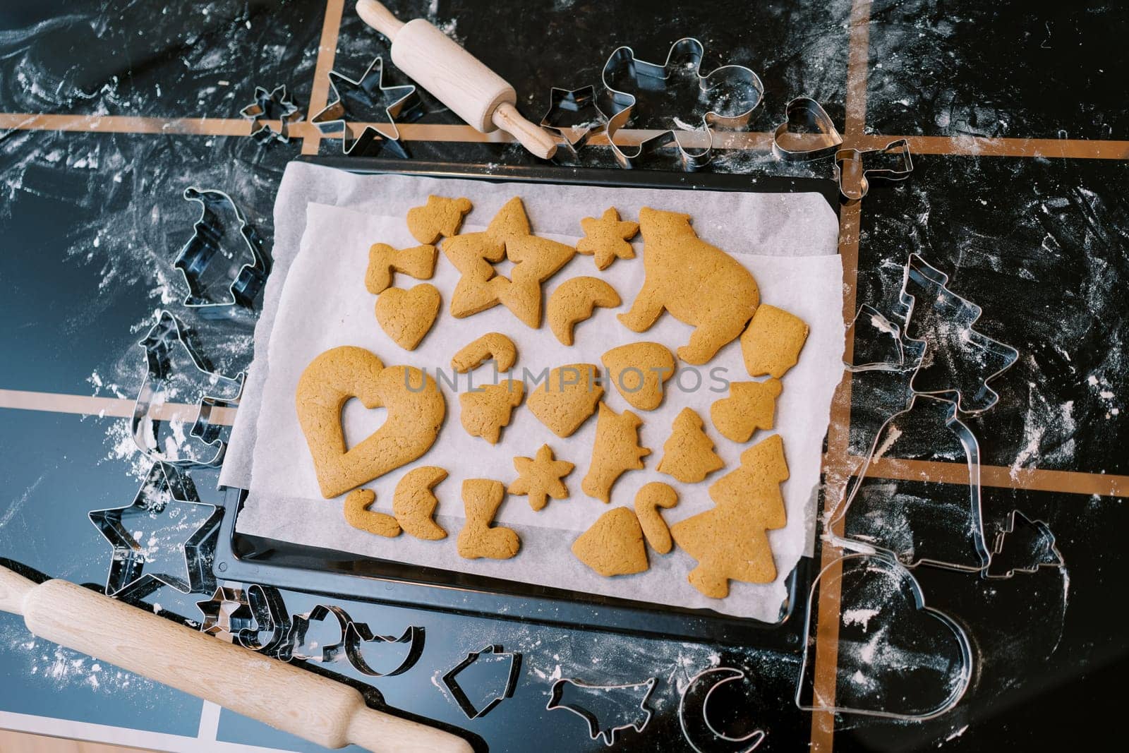 Baking tray with baked gingerbread cookies of various shapes and sizes stands on a table. Top view. High quality photo