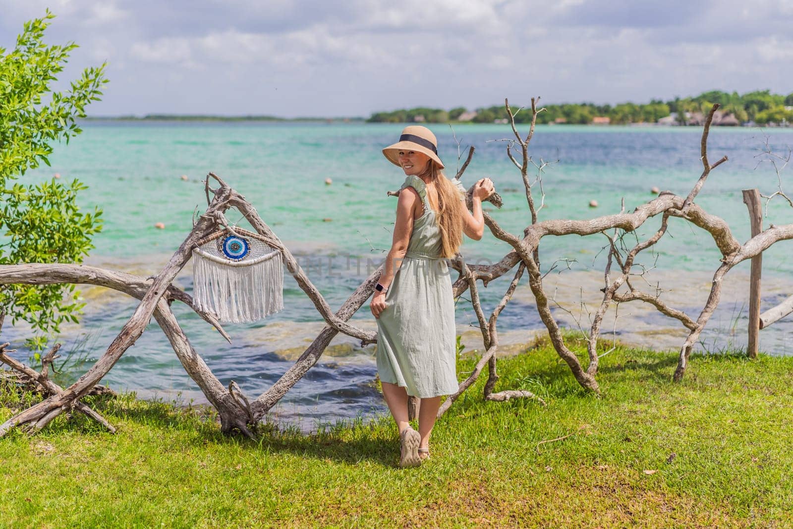 Female tourist in a turquoise dress standing on a wooden pier over the turquoise waters of Bacalar Lake, Mexico. Peaceful tropical travel destination concept.