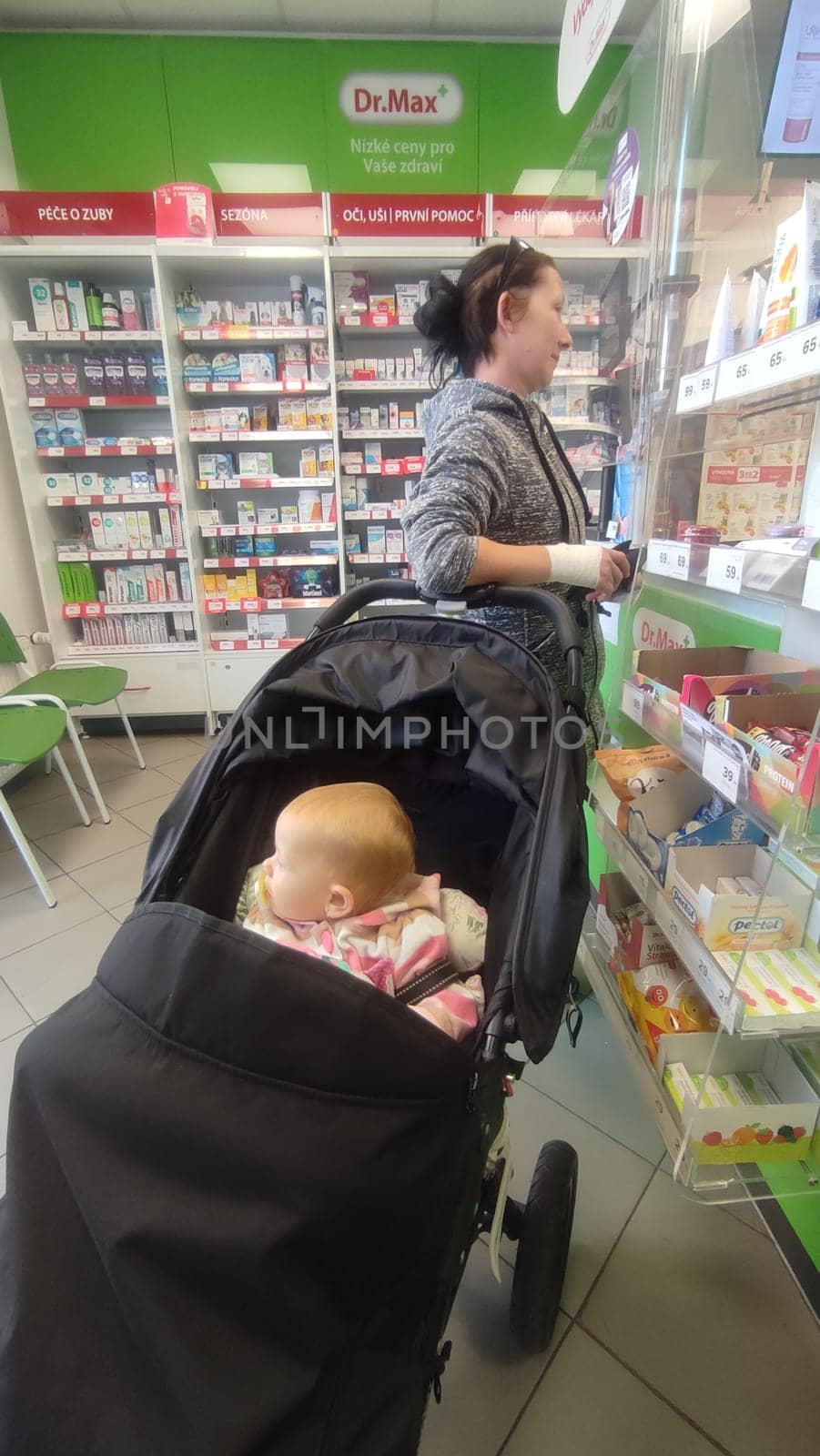 October 22 2024 Hradec Kralove, Czech Republic Europe, Kralov region, baby with pacifier sits in black stroller, child in pharmacy, medicines on shelf High quality photo