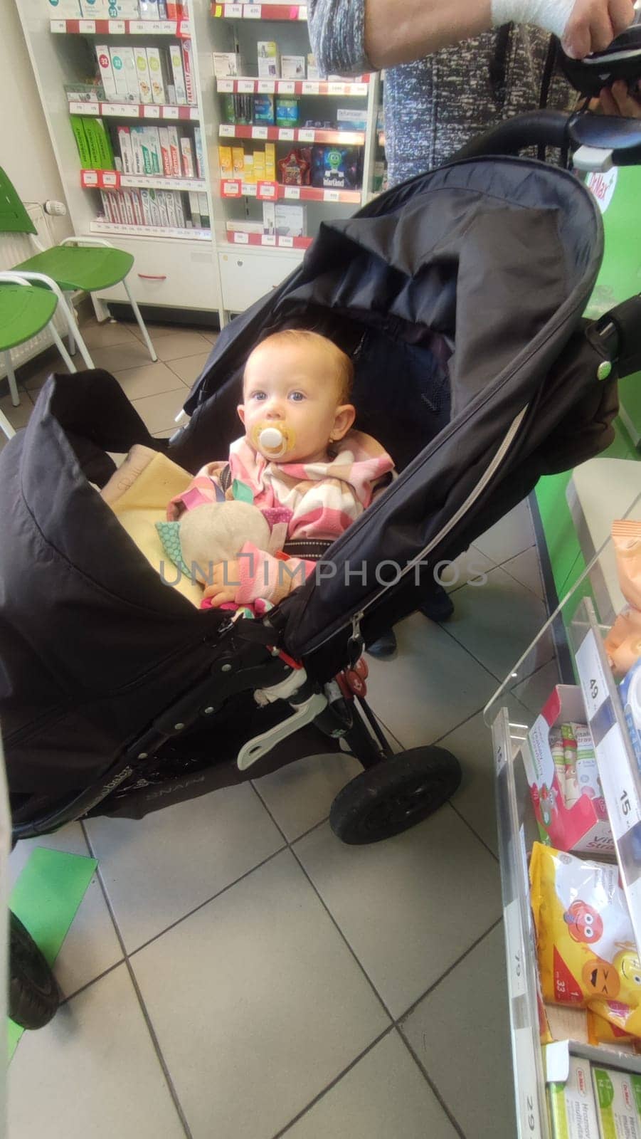 October 22 2024 Hradec Kralove, Czech Republic Europe, Kralov region, baby with pacifier sits in black stroller, child in pharmacy, medicines on shelf High quality photo