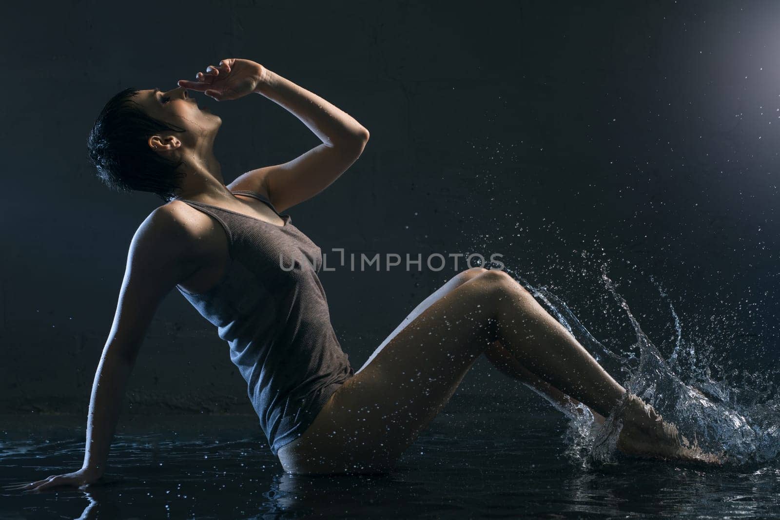 Brunette in wet t-shirt sitting under water in dark room profile portrait