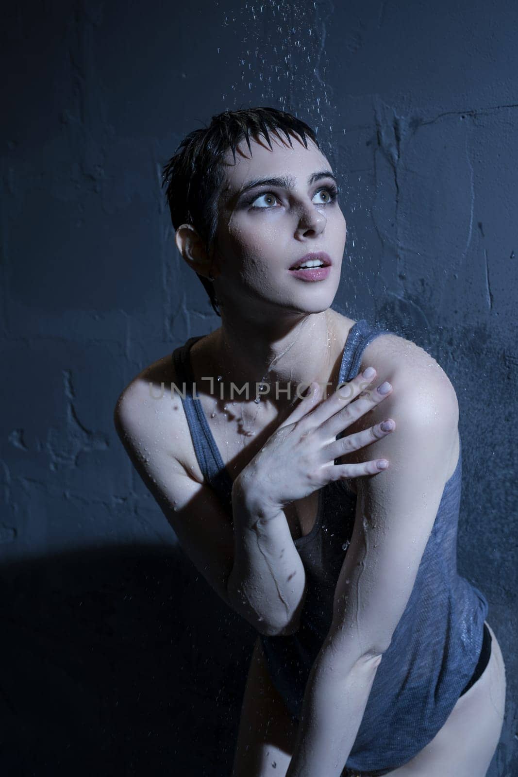 Woman in wet t-shirt standing under water in dark room portrait