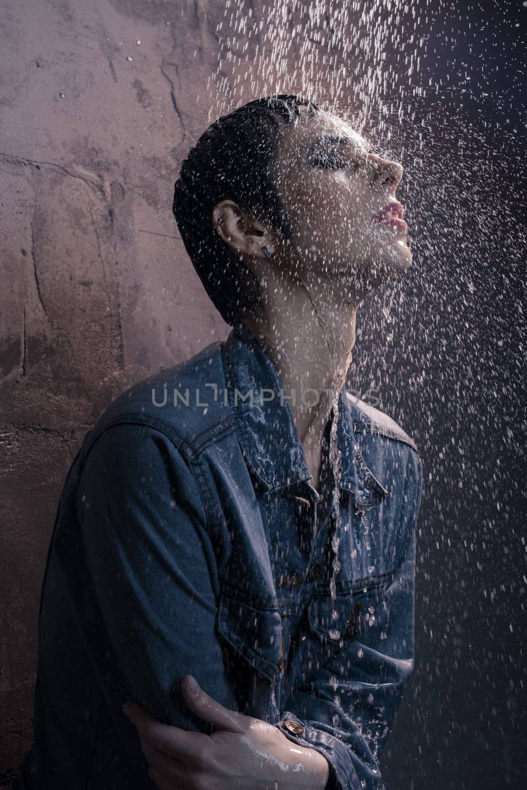 Slim brunette in jeanswear water falling on her face profile shot against brick wall