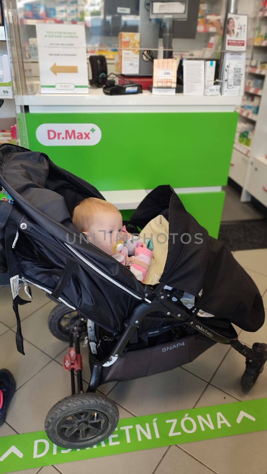 October 22 2024 Hradec Kralove, Czech Republic Europe, Kralov region, baby with pacifier sits in black stroller, child in pharmacy, medicines on shelf High quality photo