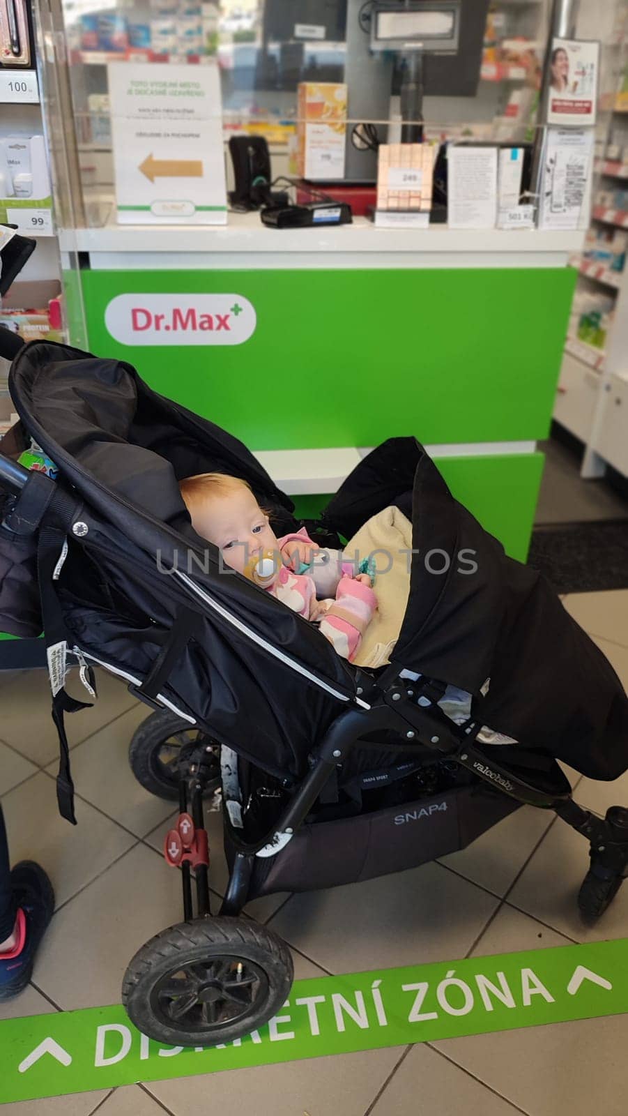 October 22 2024 Hradec Kralove, Czech Republic Europe, Kralov region, baby with pacifier sits in black stroller, child in pharmacy, medicines on shelf High quality photo