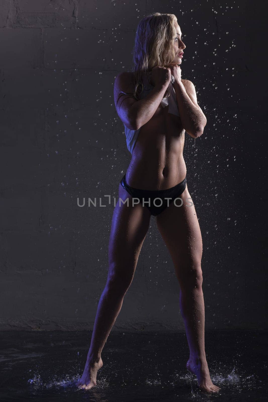 Sexy blonde in white ragged top staying under water full-length view in dark room