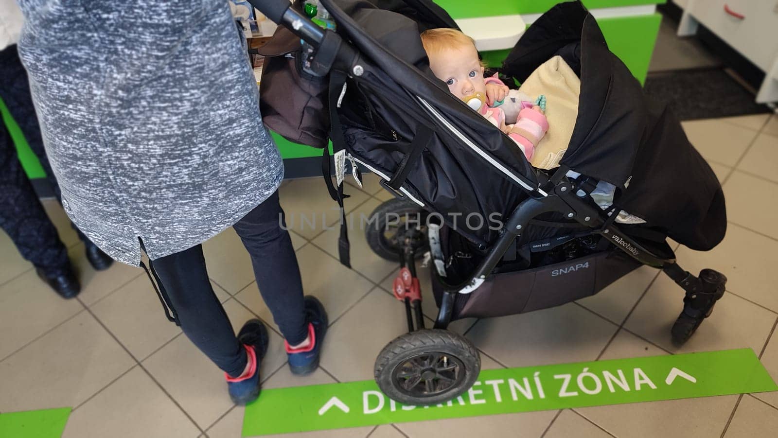 October 22 2024 Hradec Kralove, Czech Republic Europe, Kralov region, baby with pacifier sits in black stroller, child in pharmacy, medicines on shelf High quality photo