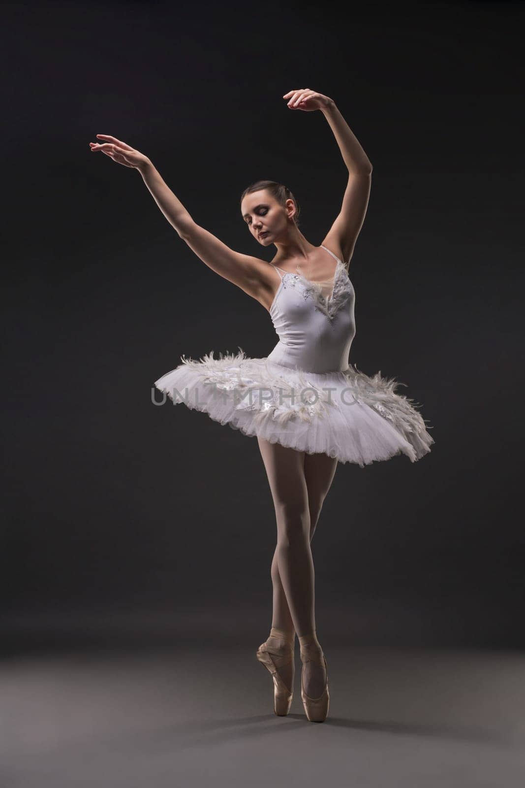 Ballerina in tutu and pointe dancing gracefully in dark room full-length shot