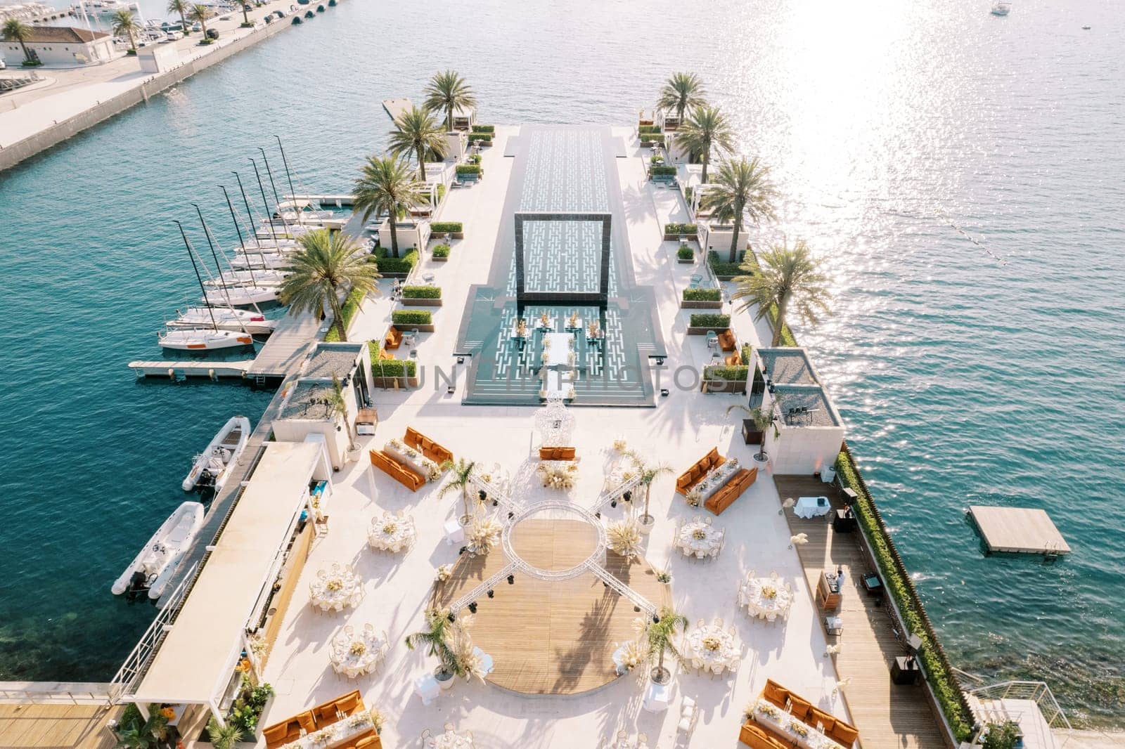 Circular stage surrounded by festive tables near a long pool on a wide pier. Top view. High quality photo