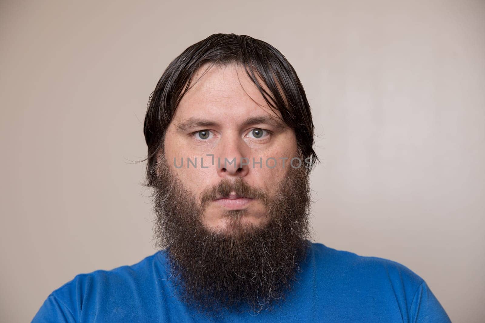 Close-up portrait of a man with a thick beard and wet hair, wearing a blue shirt, against a neutral background.