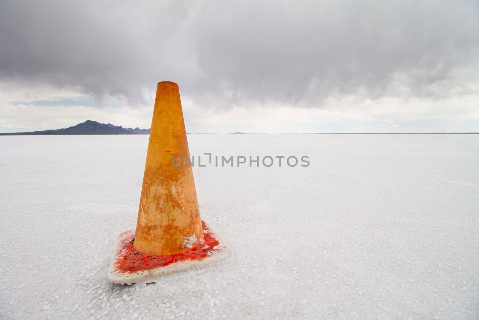 An orange traffic cone stands alone on an expansive salt flat. The scene captures isolation, tranquility, and the unusual contrast between the vibrant cone and the muted landscape.