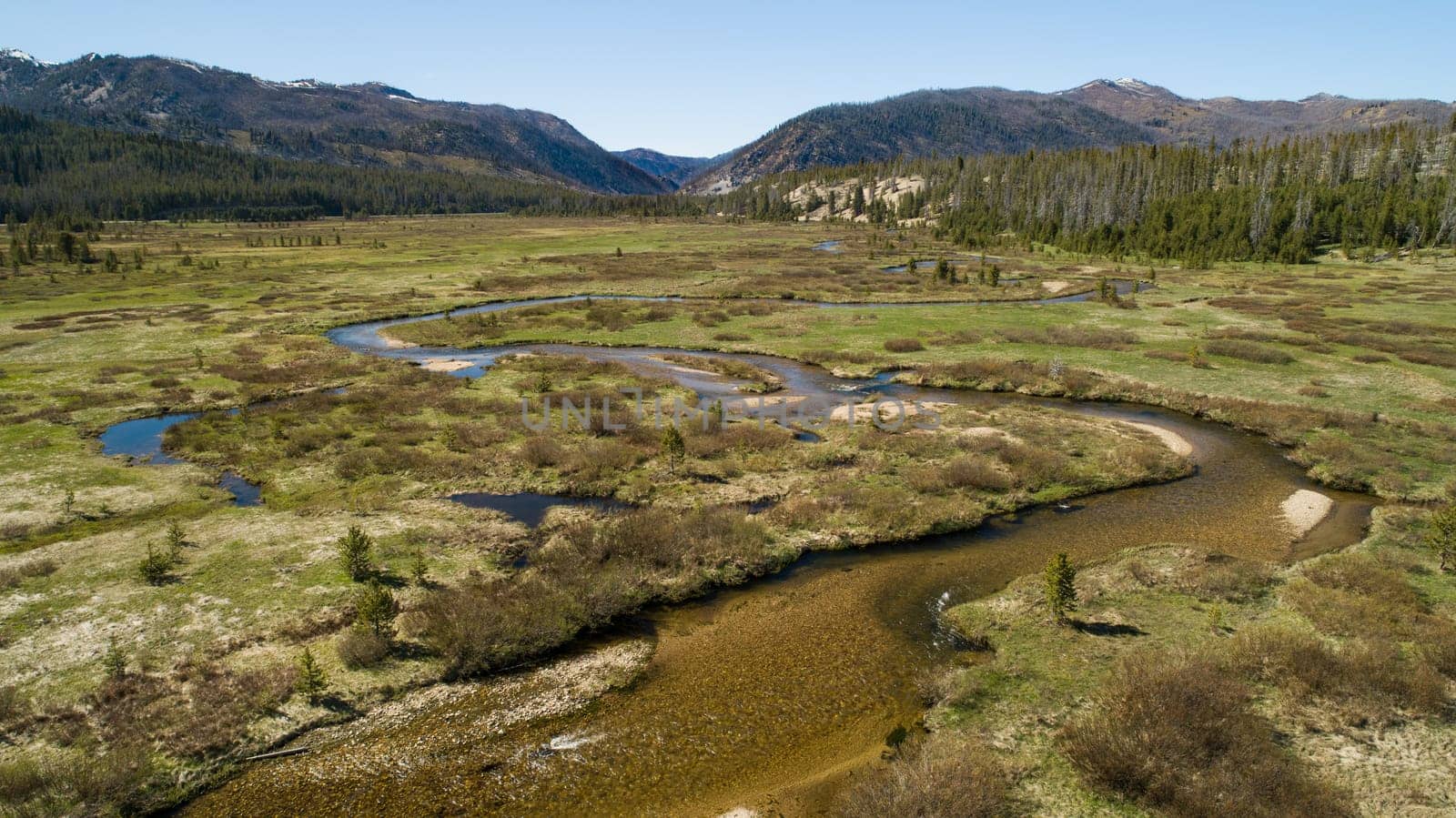 A breathtaking aerial view of a tranquil mountain valley featuring a winding river surrounded by lush greenery and distant mountains under a clear blue sky in stanley idaho