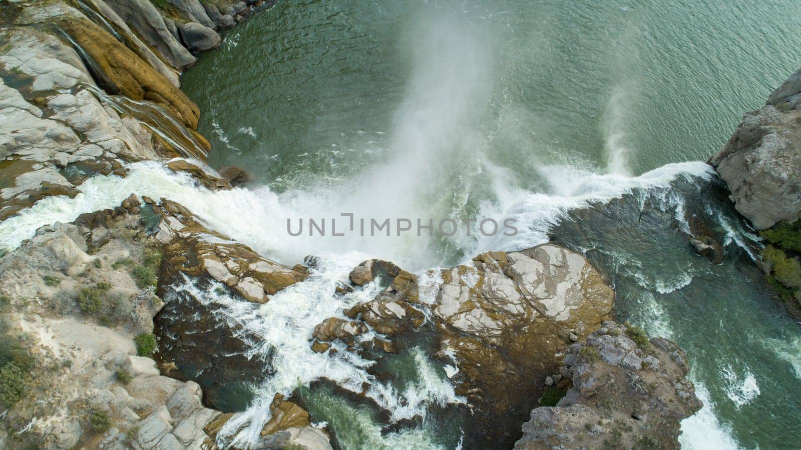 Captivating aerial view of a powerful waterfall cascading over rugged rocks into a serene body of water, surrounded by natural beauty at shoshone falls in twin falls