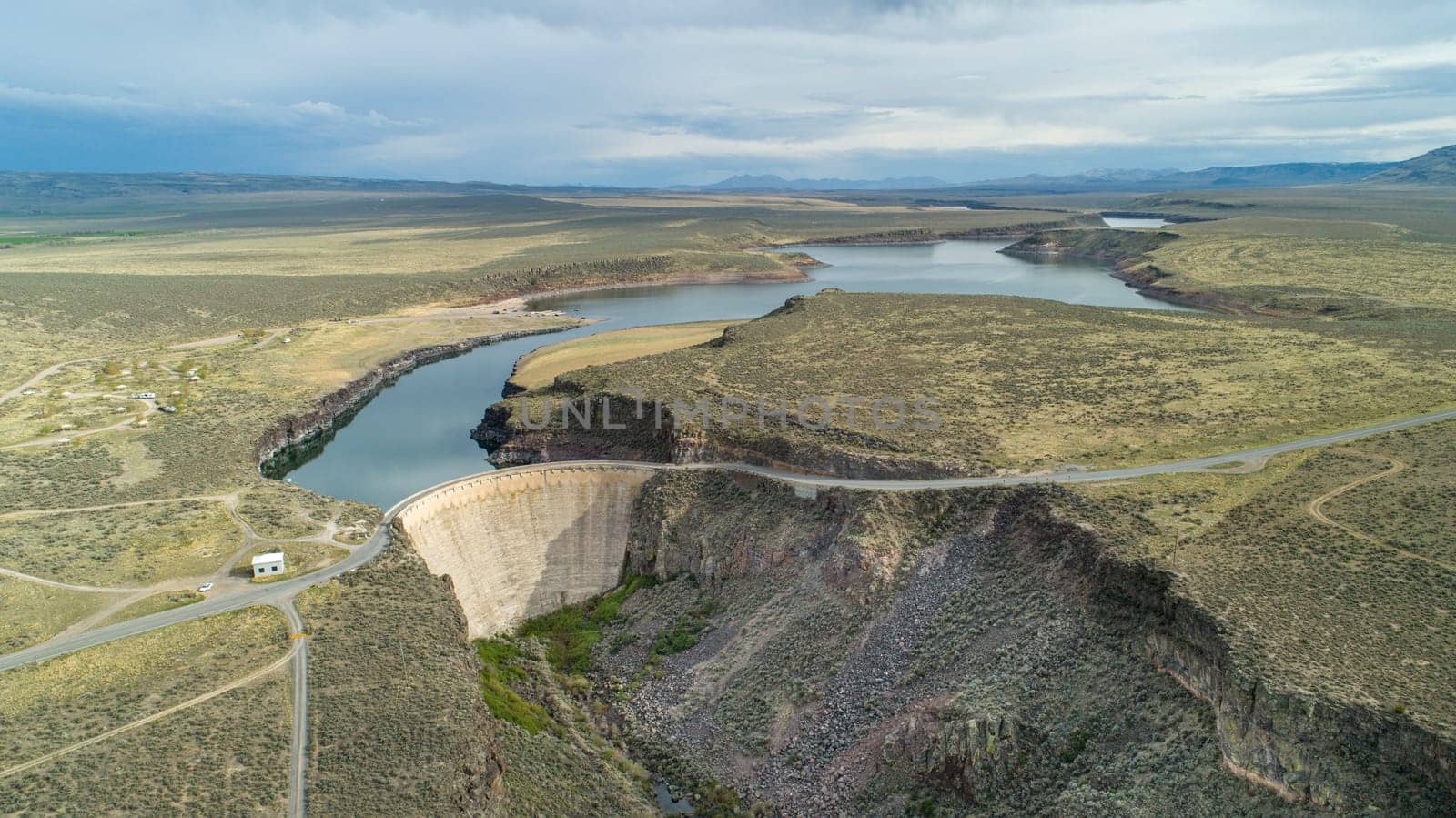 Aerial panorama of a vast landscape showcasing a scenic dam surrounded by a winding river and expansive terrain. An ideal depiction of natural beauty and engineering.