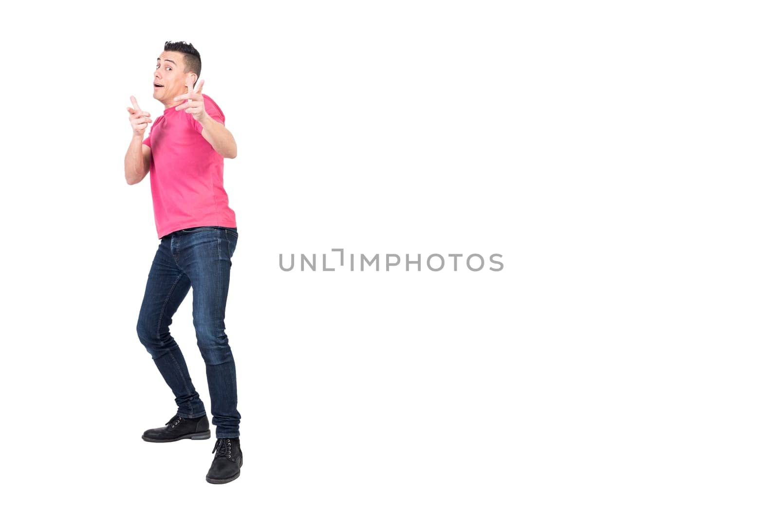 Full body of young funny male model with dark hair in pink t shirt and jeans looking and pointing at camera against white background