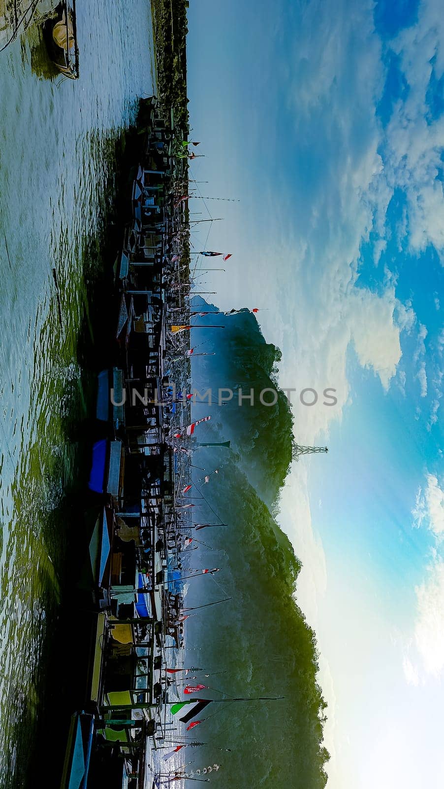A large group of boats are floating on a lake. The sky is blue with some clouds
