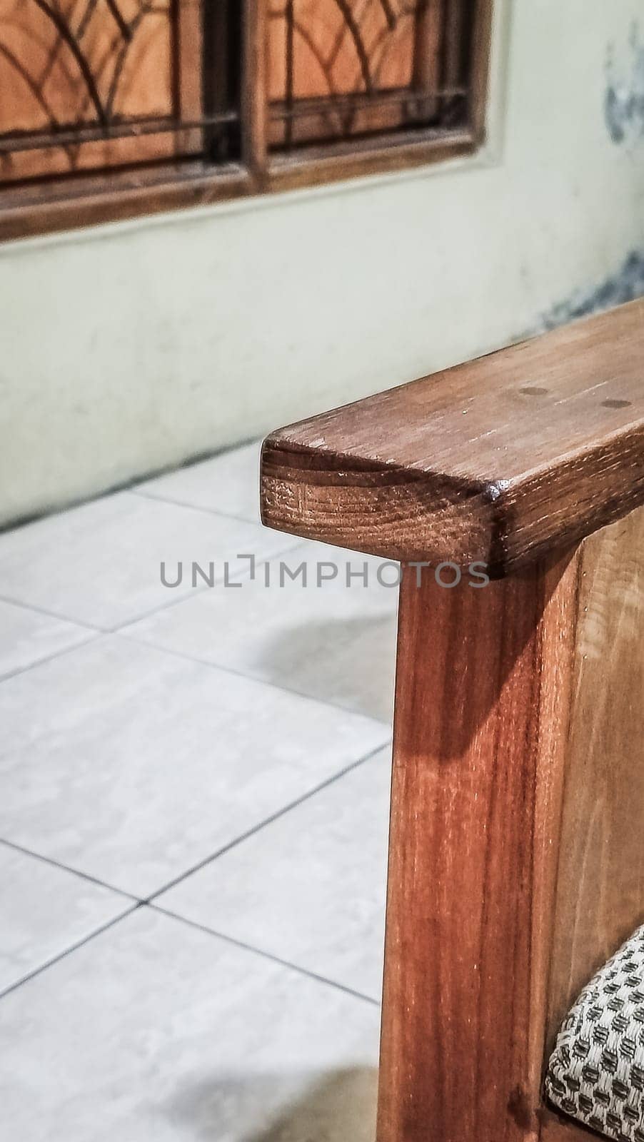 A detailed view of a wooden chair armrest, highlighting its texture and design. The cozy indoor setting includes tiled flooring and a window.