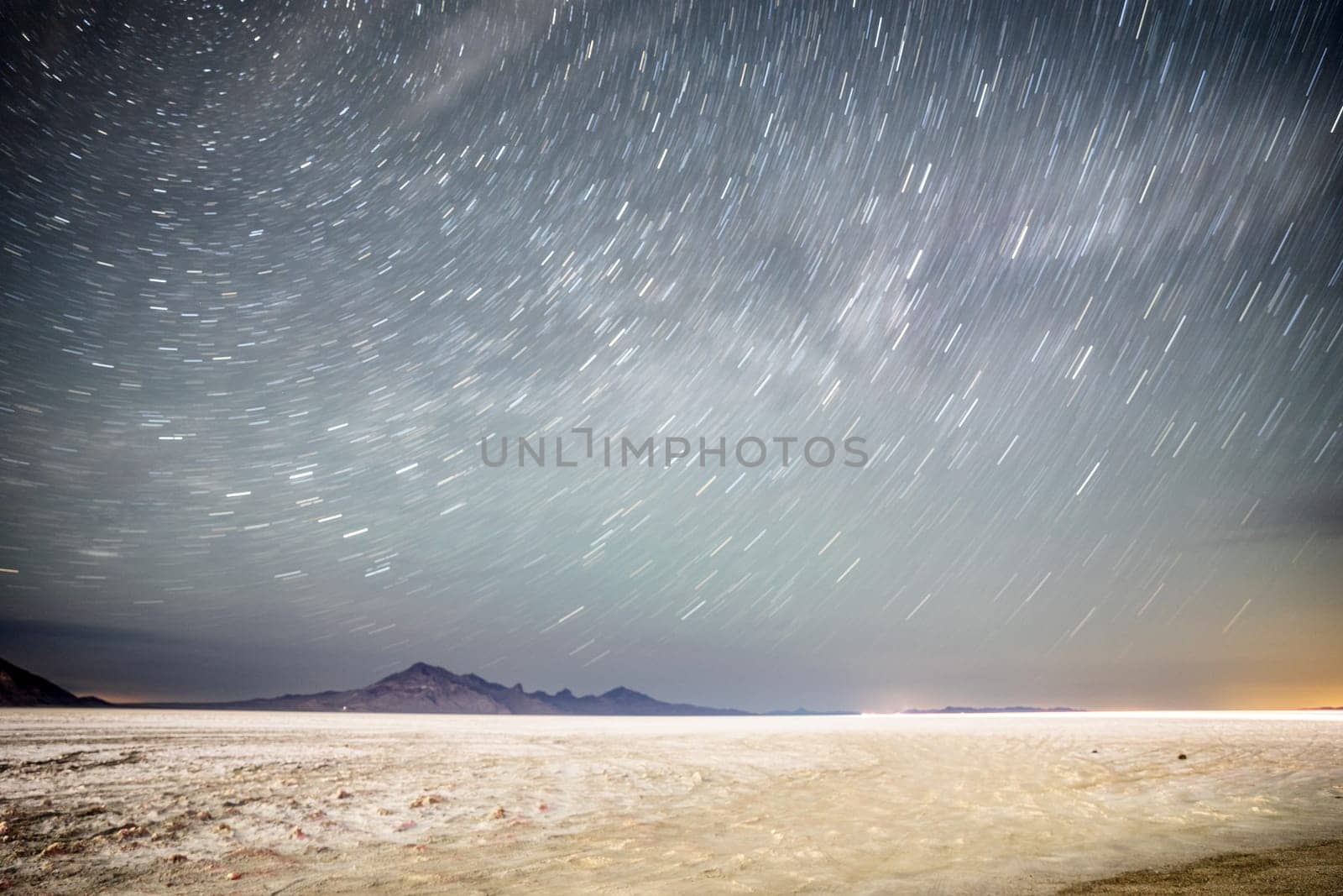 Mesmerizing star trails in the night sky over a serene desert landscape, showcasing the vastness and tranquility of nature. Captures the essence of the universe in motion.