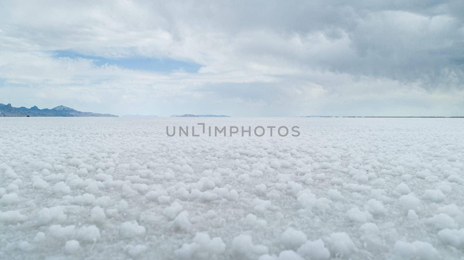 A wide view of expansive white salt flats under a cloudy sky, with distant mountains visible on the horizon, creating a serene and tranquil landscape.
