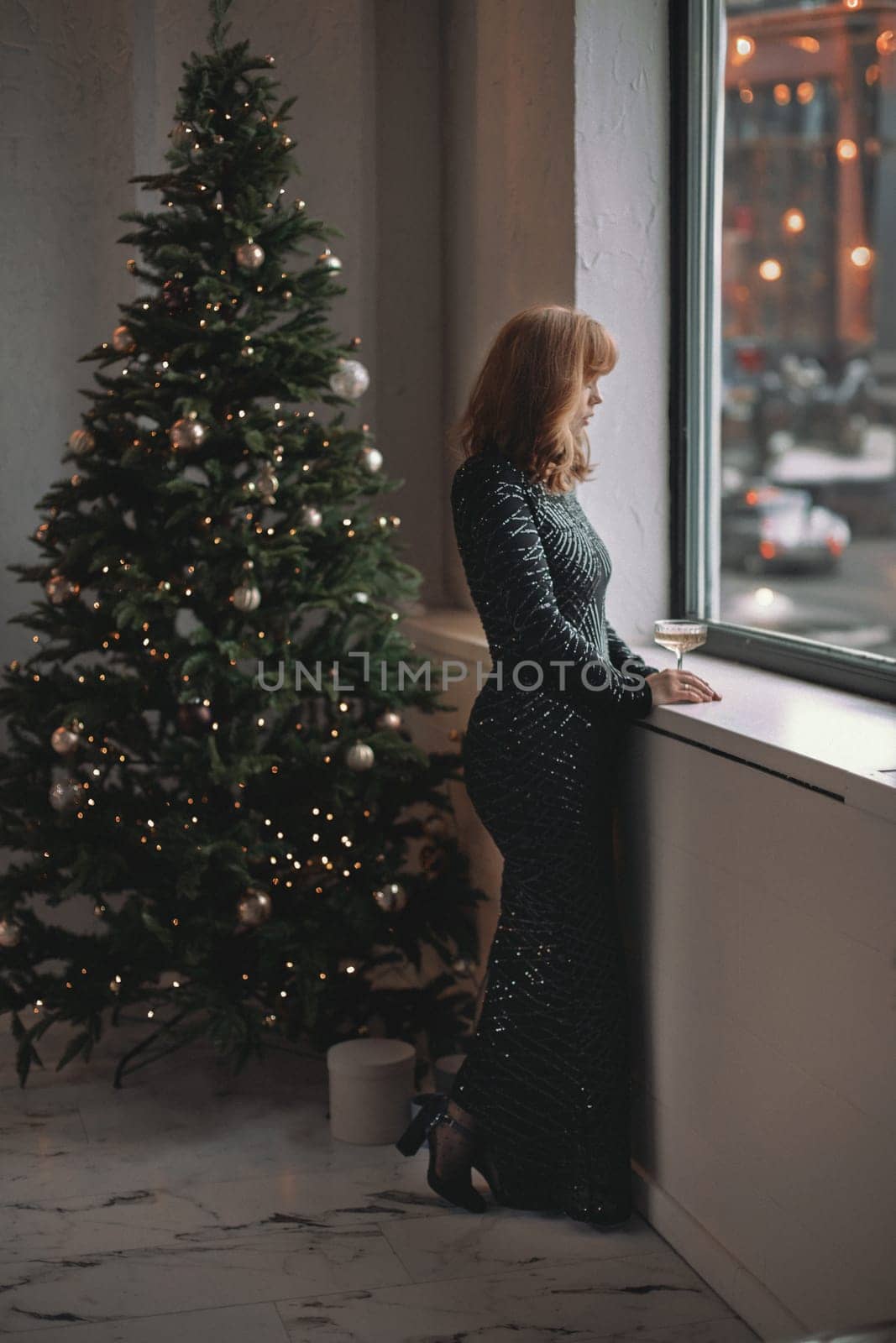 A beautiful elegant woman in a long dress next to the Christmas tree. Christmas and New Year holidays.