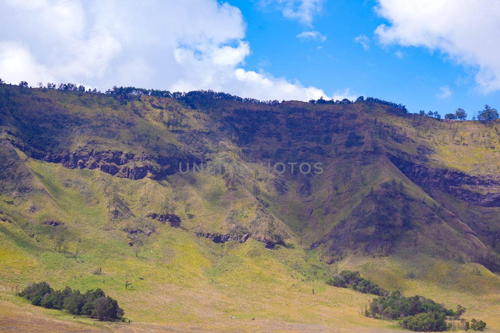 A picturesque landscape of rolling hills with vibrant green grass under a dramatic blue sky and fluffy white clouds.