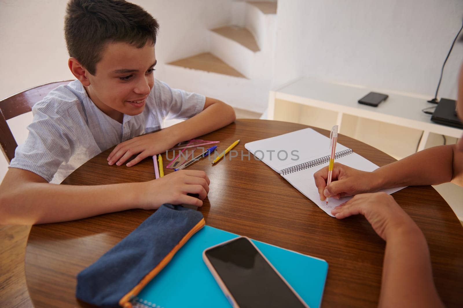 Young boy smiles while collaborating with an adult at a table filled with notebooks and school supplies, fostering learning and education.
