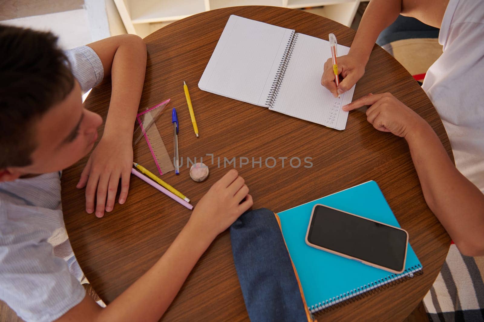 Two students work together on a homework project, using notebooks and pencils at a round table, emphasizing collaboration and learning.