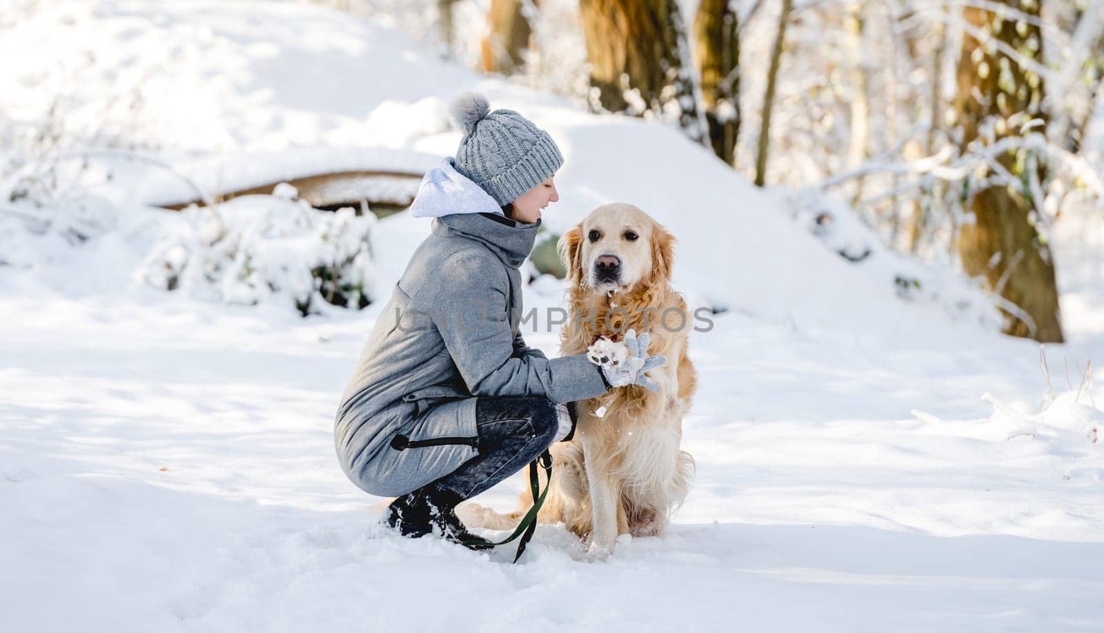 Teenage Girl And Golden Retriever Sit Together In Snow-Covered Forest During Winter