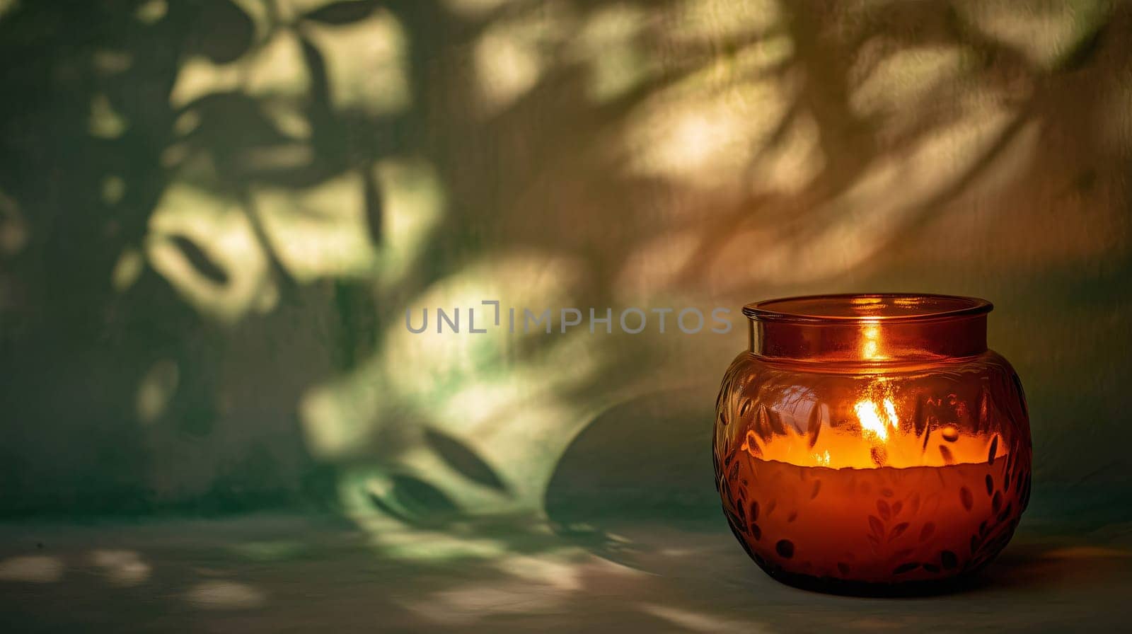 Amber candle burning in a glass jar, with botanical shadows cast on the wall behind it