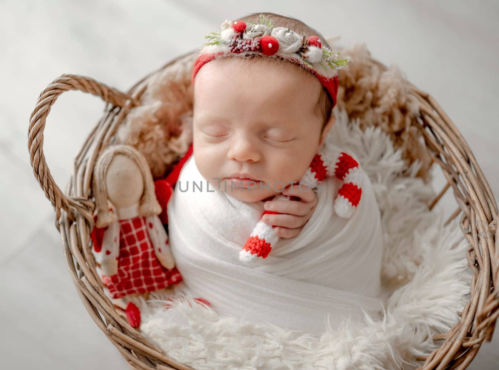 Baby Girl Sleeps In Basket In Christmas Attire With Candy Toy During Newborn Photoshoot In Studio