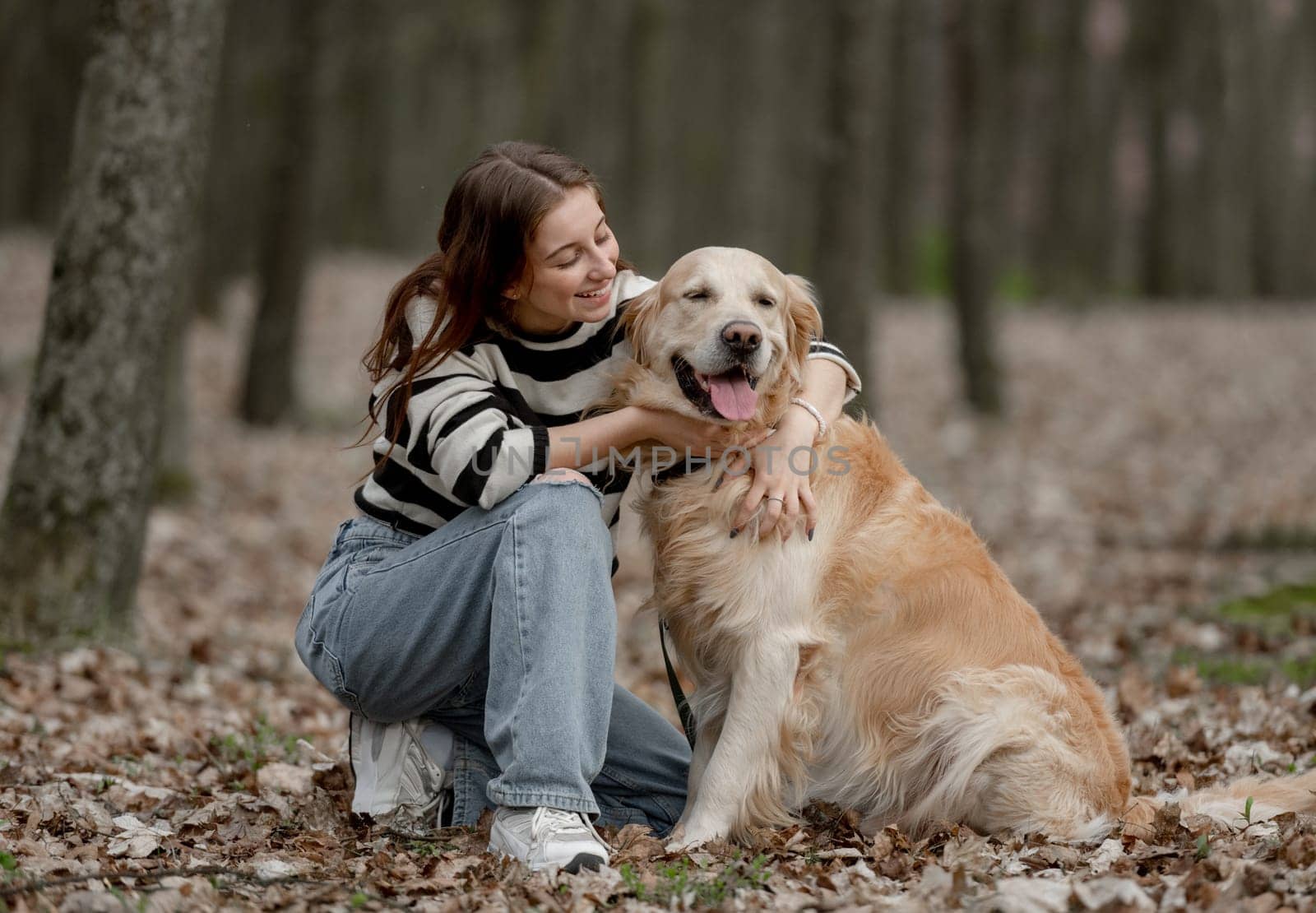 Teenage Girl Sits With Golden Retriever In Park During Autumn