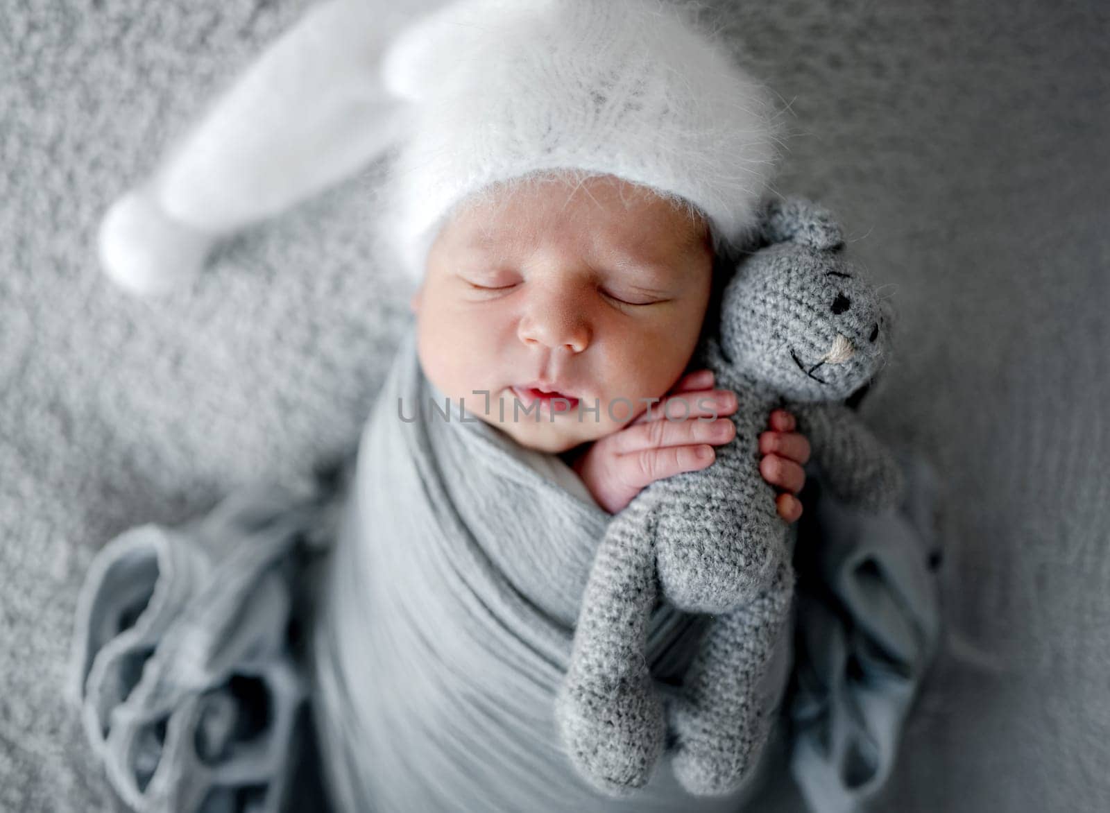 Newborn Baby Sleeps In Grey Wrap With Bunny Toy During Photoshoot