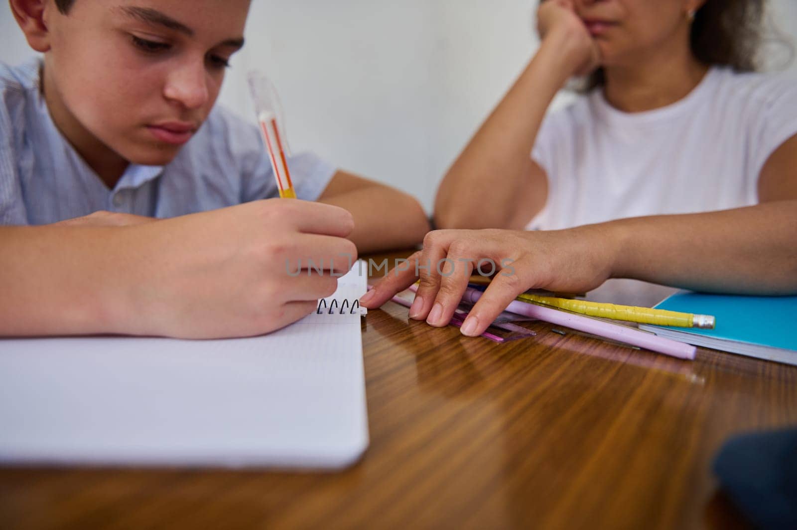 A young boy intensely writes in a notebook while his mentor looks on. The setting conveys focus and the importance of one-on-one learning, highlighting educational mentorship.